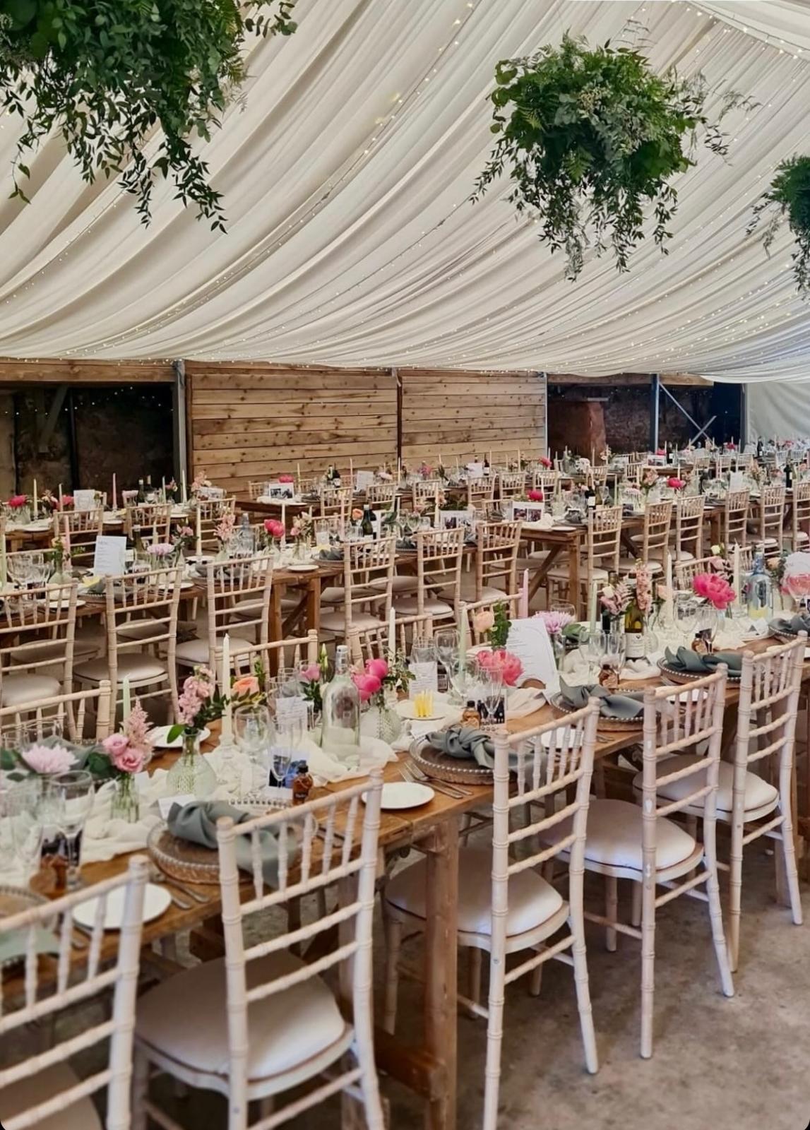 Rustic wooden trestle tables with crossback chairs in a marquee
